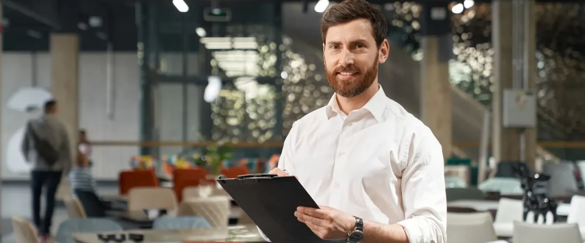 Successful handsome restaurateur smiling at camera, while choosing furniture in store.